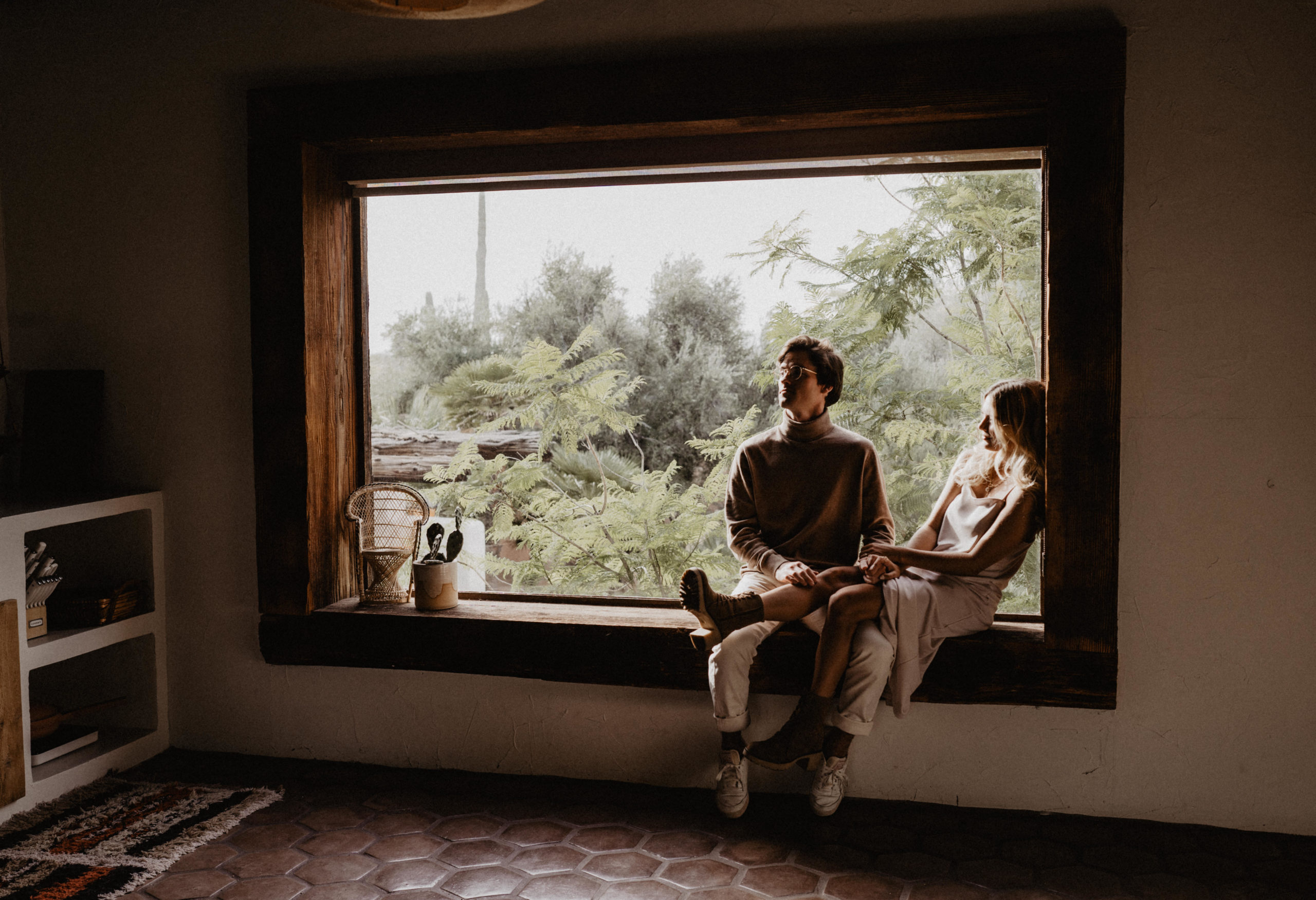 Couple sitting in a window with trees in the background.