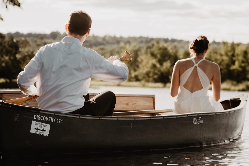 Bride and Groom paddle  in a canoe off from their lakeside elopement immediately after their ceremony in Maine.