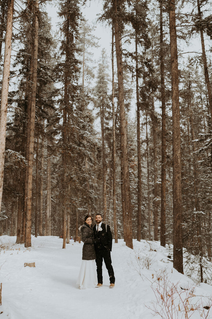 Bride and groom stand in a forrest of towering trees during their adventure elopement. 