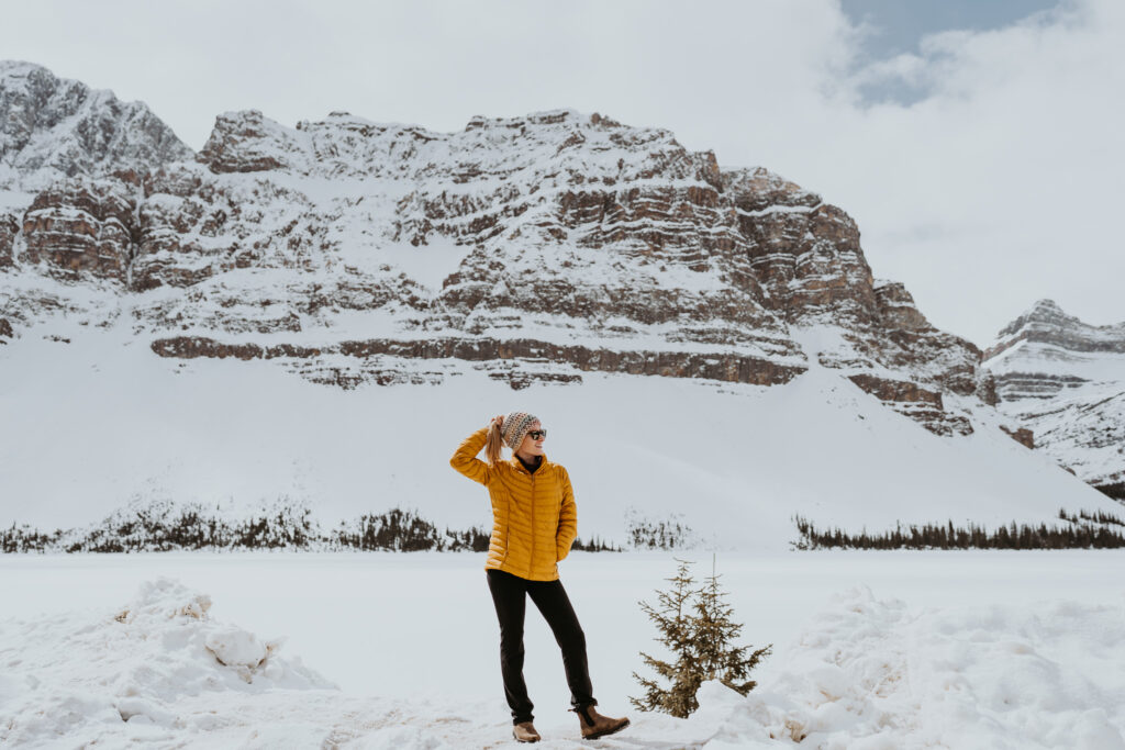 Adventure Elopement Photographer in a yellow jacket stands in the snowy base of a mountain looking to her left 