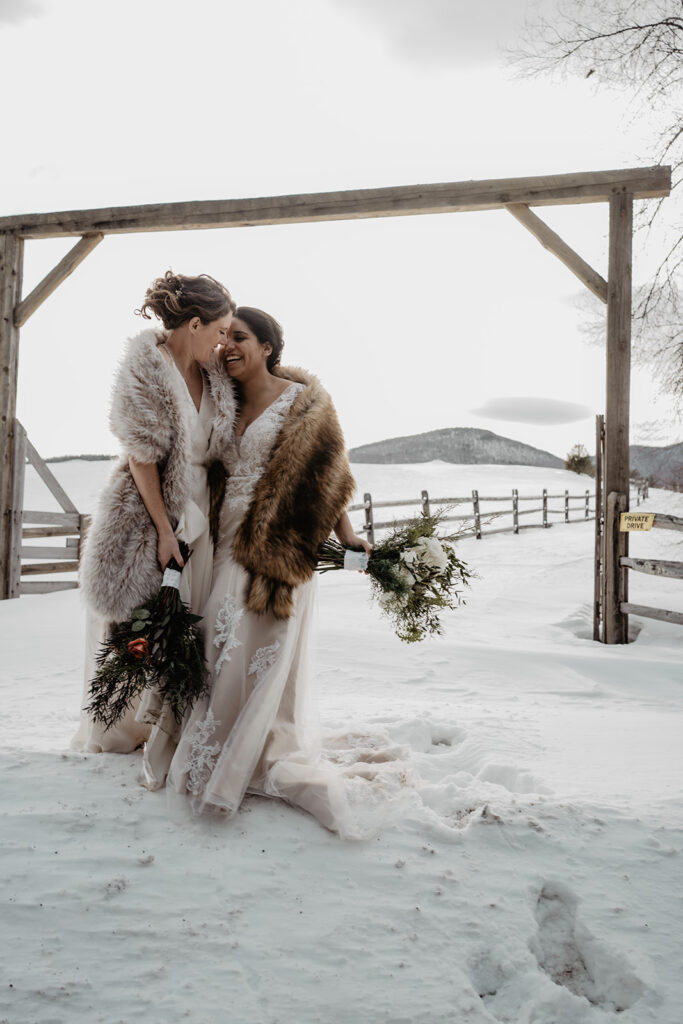 Brides lock eyes as they embrace at the entrance to a snowy farm during their New England Elopement. 