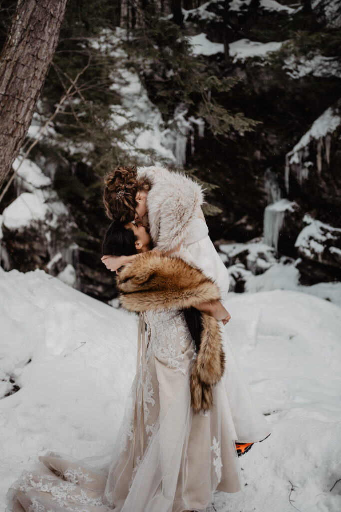 Bride is held up by her bride in a snowy forrest during their New England Elopement. 