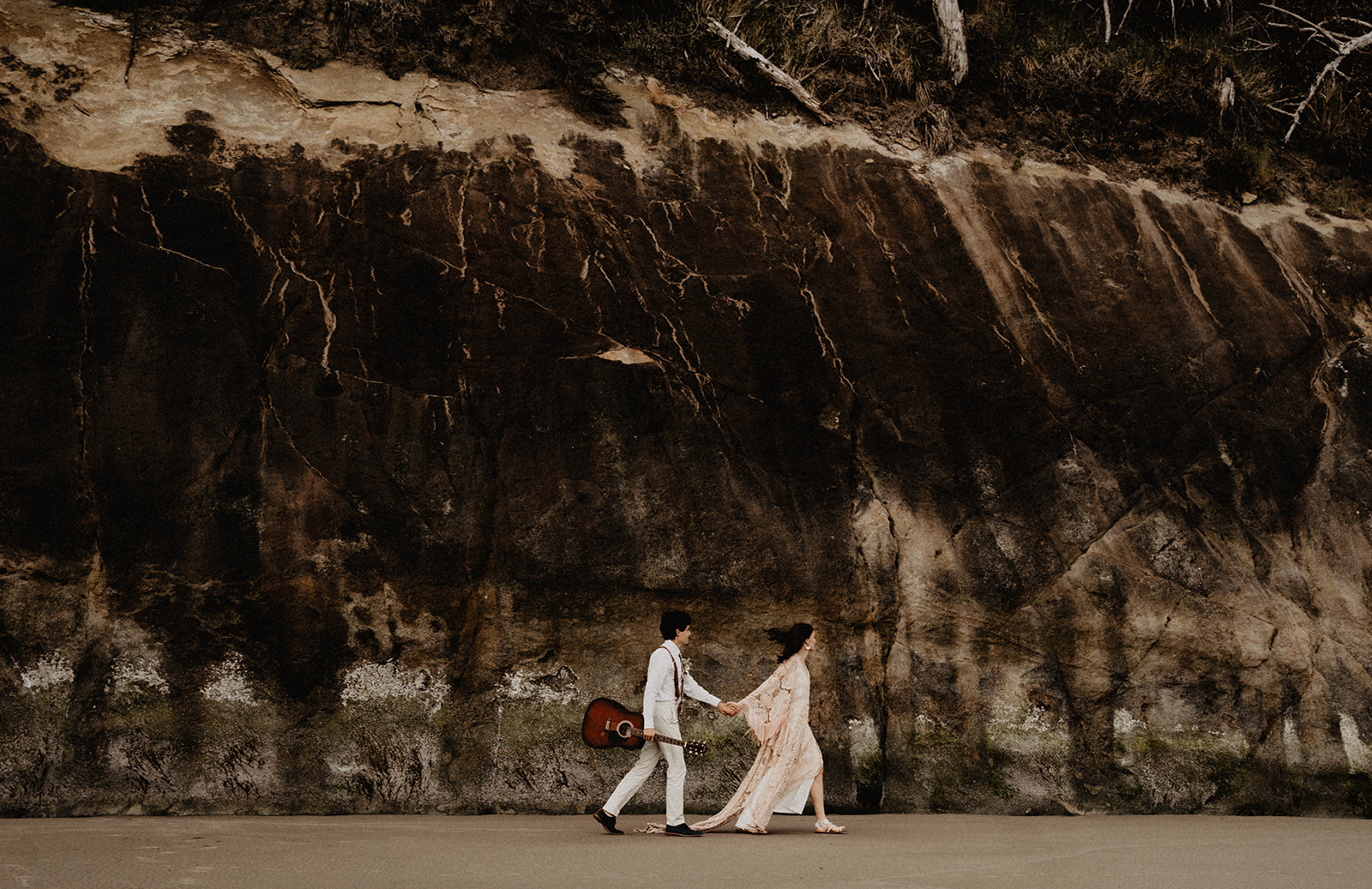 Bride leads groom along a rocky shore during their destination elopement.