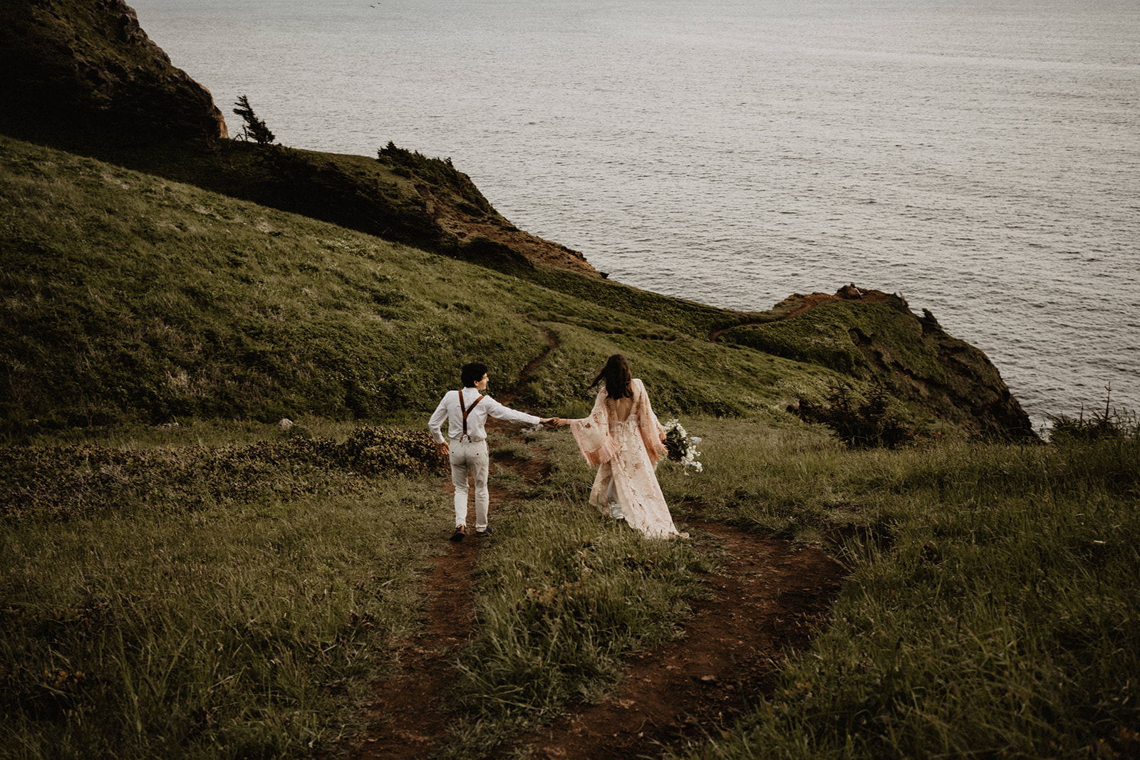 Bride and groom run through a grassy, beachside meadow during their destination elopement.
