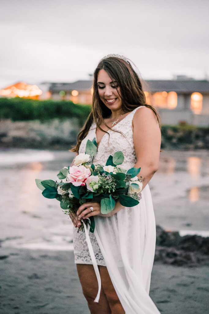 Bride gazes at her bouquet on the wet sands of the beach during her New England Elopement. 