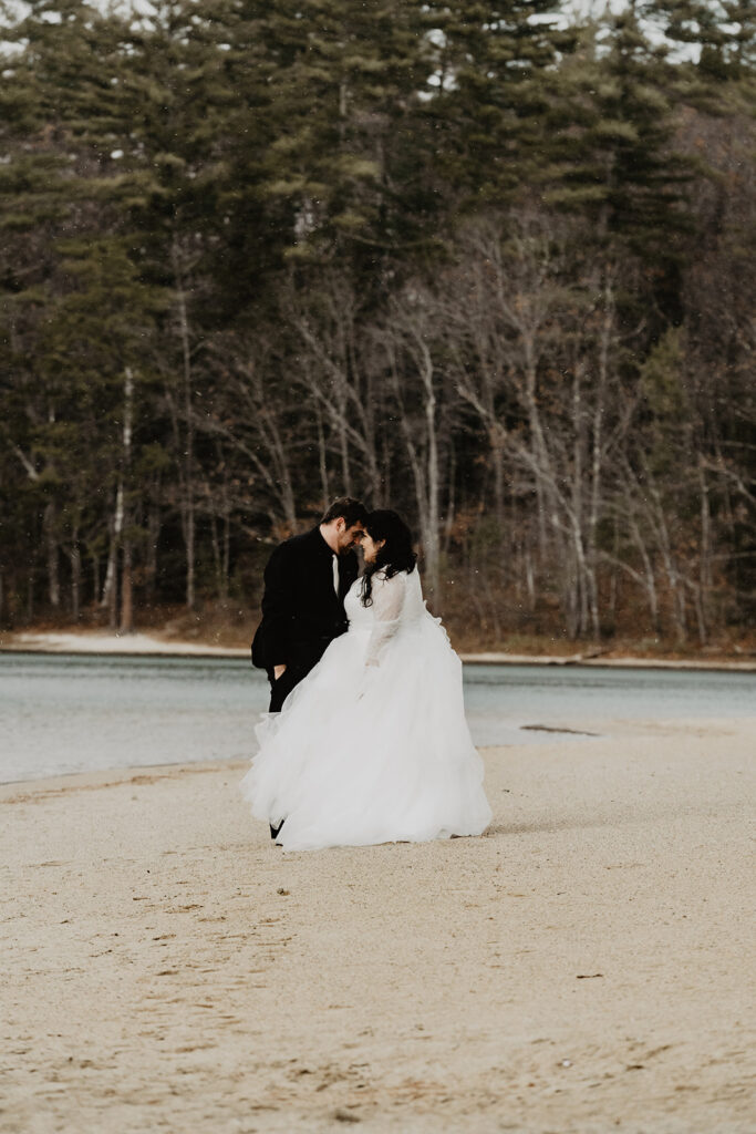 Bride and groom stand, leaning their foreheads against each other on the sandy shore during their New England Elopement. 
