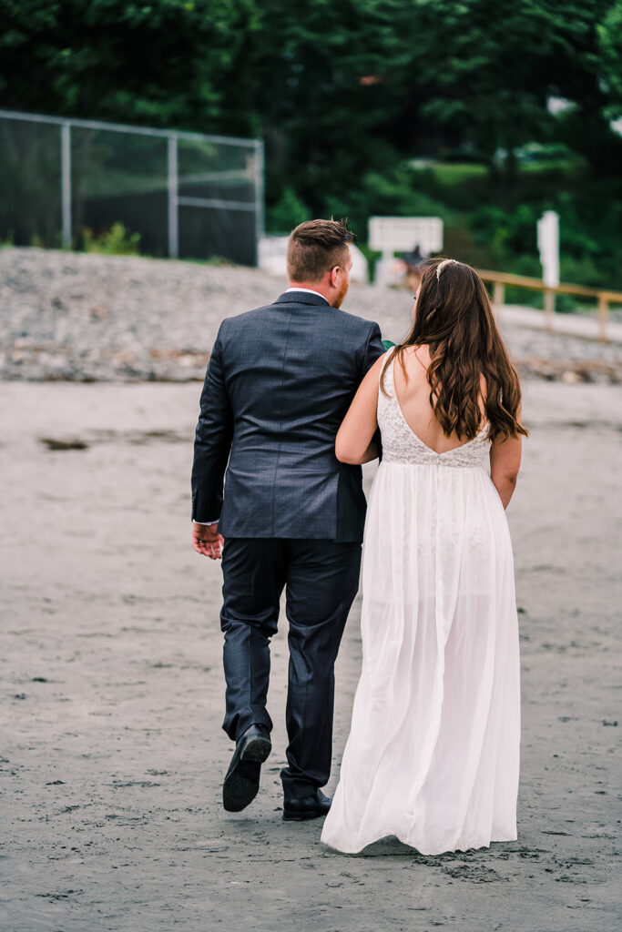 Bride and groom walk arm in arm in the sand during their New England Elopement. 
