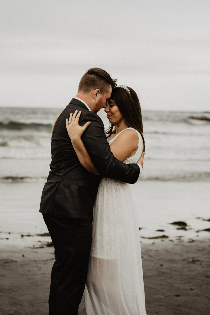 Bride and groom embrace and dance in the sand with waves crashing in the background during their New England Elopement. 