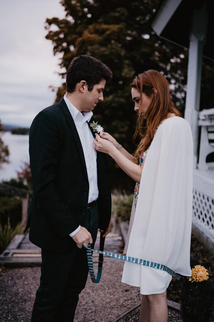 Bride pins boutonnière on groom at their New England Elopement. 