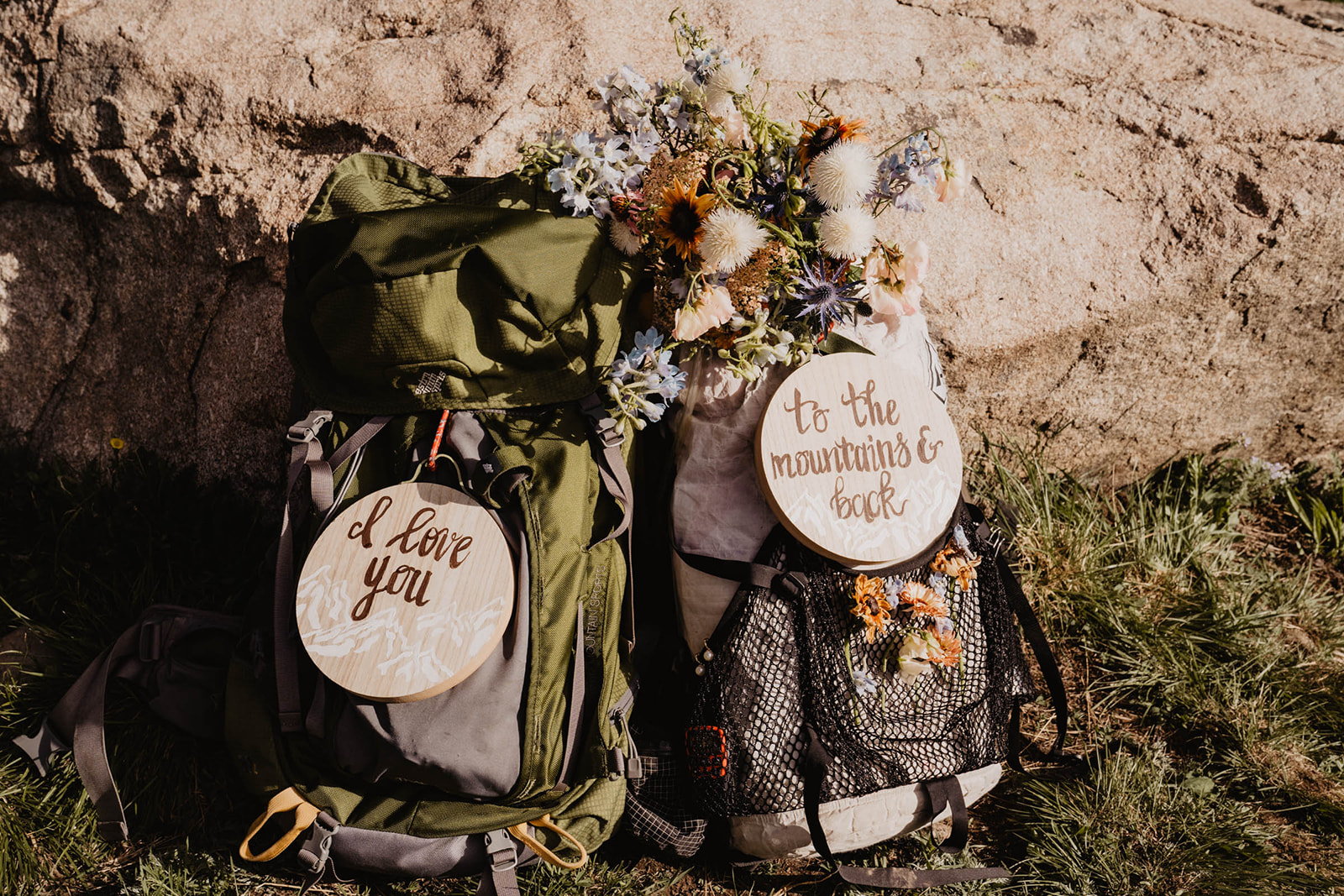 Two hiking packs decorated with flowers, and wooden signs that read "I love you" and "to the mountains"