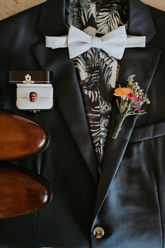 Groom's attire is laid out with boutonniere, bow tie, shoes and jewelry box. 