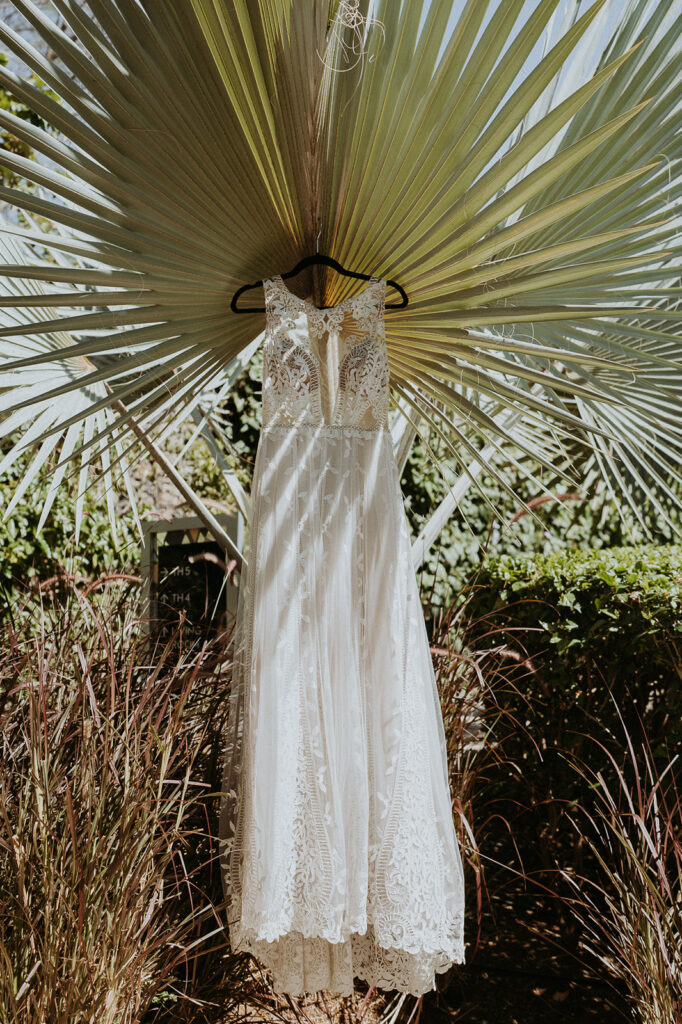 White lace dress is hung juxtaposed with green palms during a Costa Rica destination wedding. 