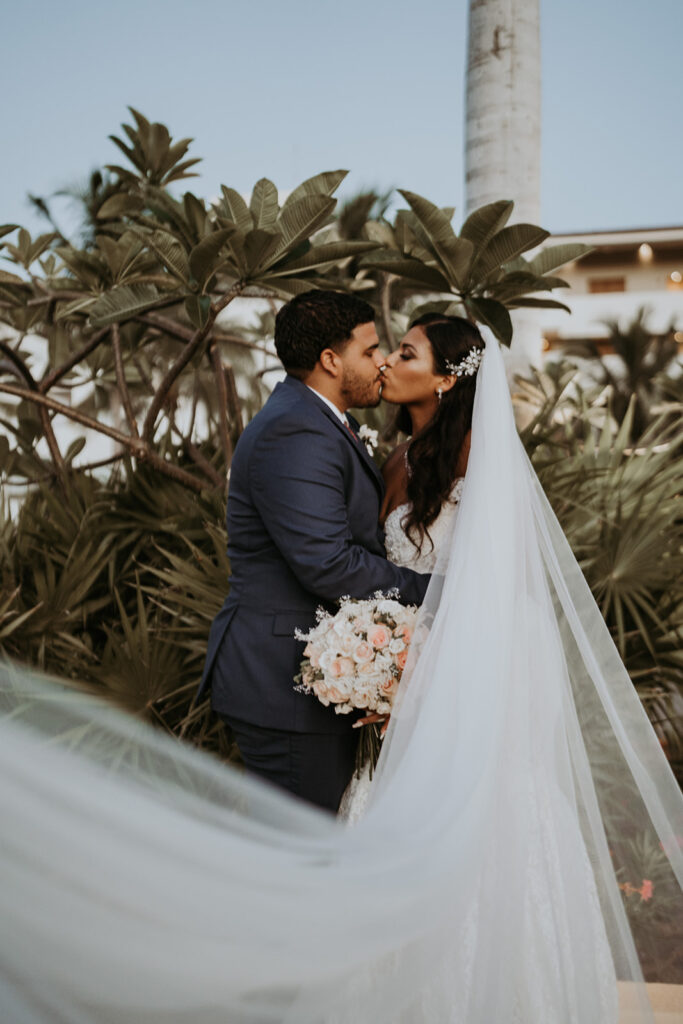 Bride and groom kiss in front of palm trees during their destination wedding in Mexico.